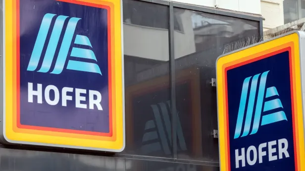 Zwei Schilder der Supermarktkette Hofer sind an einer Fassade angebracht.
